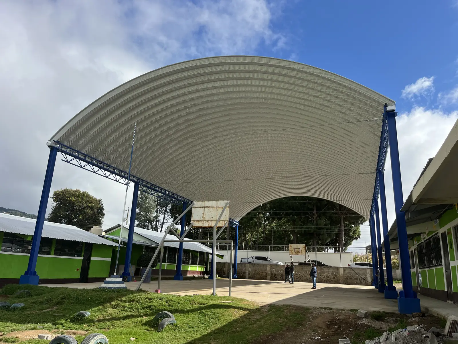 Cancha escolar con techo curvo de lámina y columnas azules