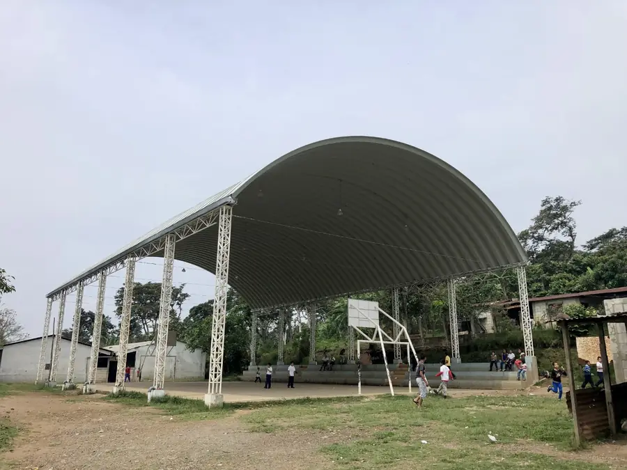 Cancha comunitaria techada con techo curvo sobre columnas de celosía